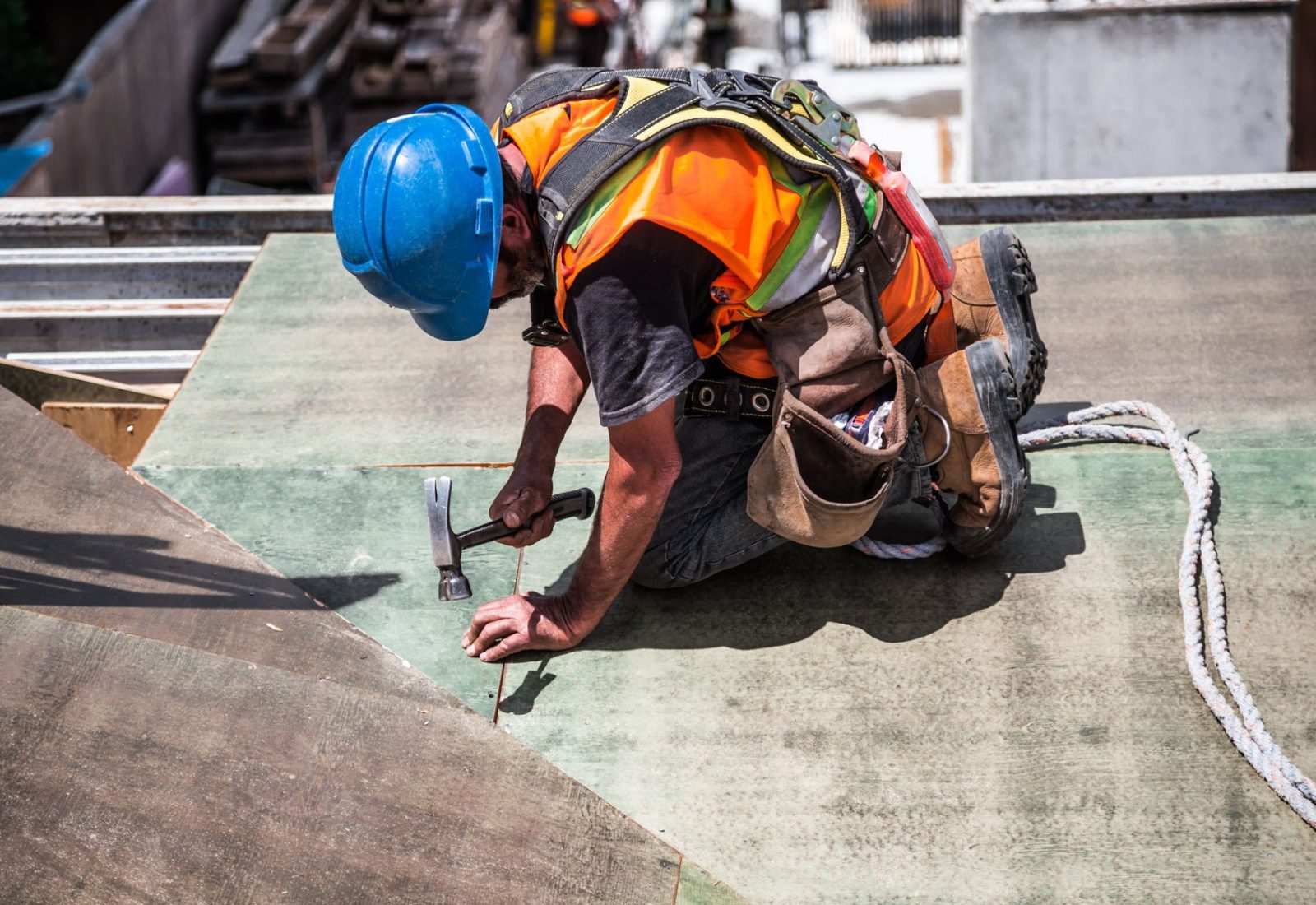 Dachdecker mit Helm und Werkzeuggürtel arbeitet kniend an der Dachabdichtung