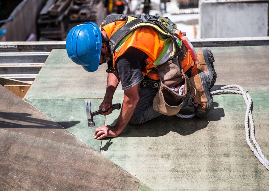 Dachdecker mit Helm und Werkzeuggürtel arbeitet kniend an der Dachabdichtung
