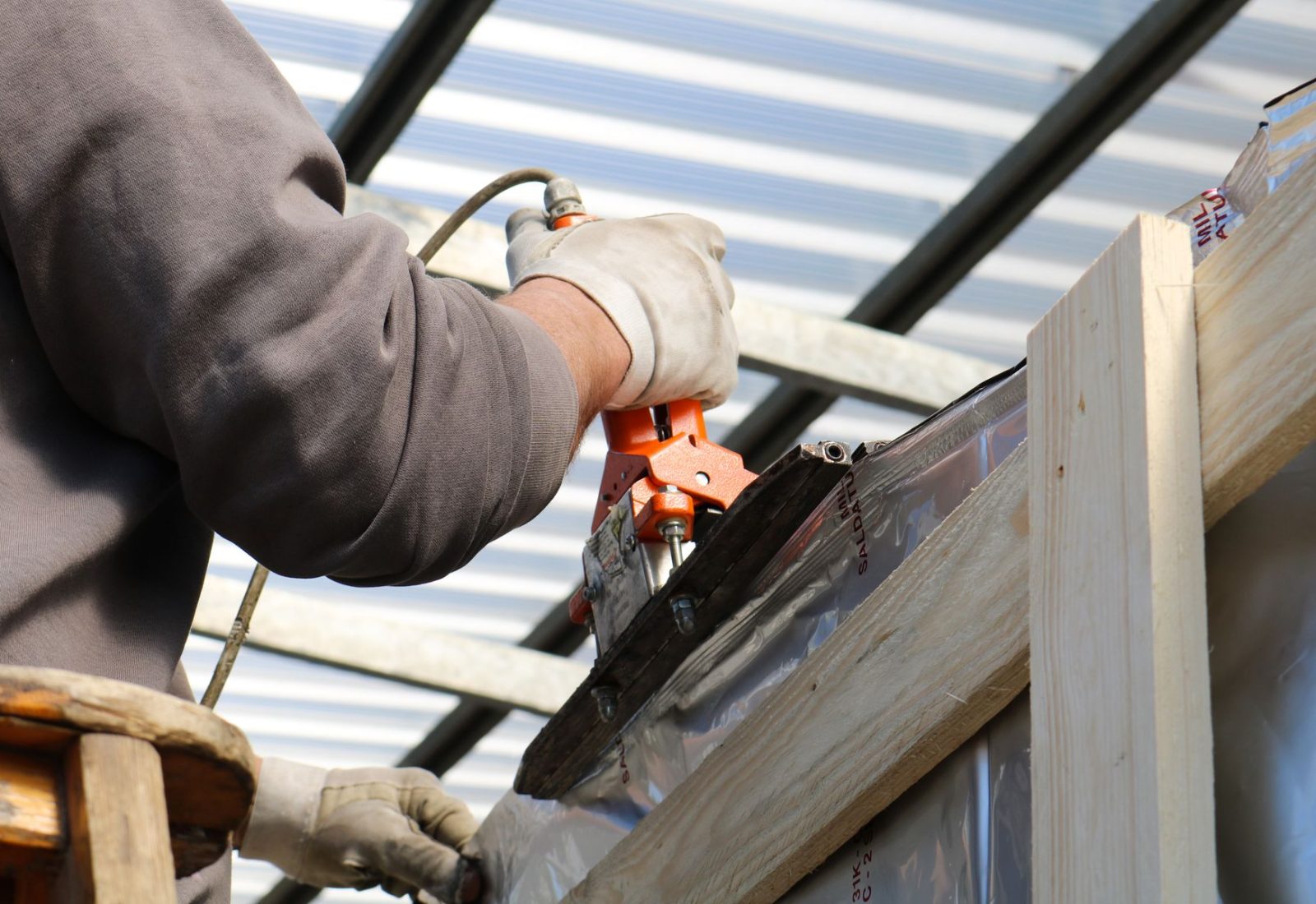 Handwerker bearbeitet mit Werkzeug eine Metallverkleidung an einer Dachkonstruktion