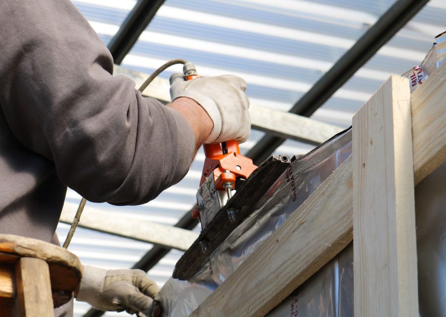 Handwerker bearbeitet mit Werkzeug eine Metallverkleidung an einer Dachkonstruktion